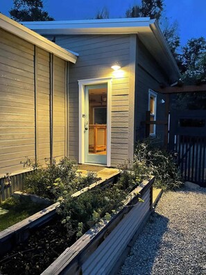 A residential building with a front door, a small porch, and a garden area with plants and a wooden bench.
