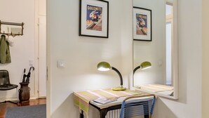 Un petit bureau avec un bureau, deux lampes, une chaise, un miroir et deux affiches encadrées accrochées au mur.