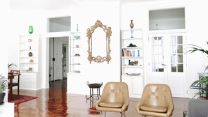 Un vaste salon doté d’un plancher en bois, de deux fauteuils en cuir, d’un grand miroir décoratif et d’étagères blanches où sont disposés divers objets décoratifs.