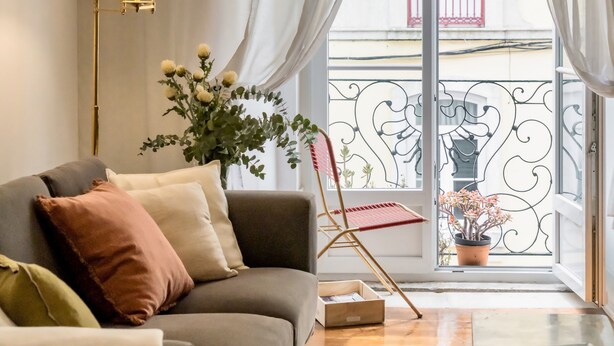 Un salon avec un canapé, une lampe sur pied, une plante en pot et une vue sur un balcon doté d’une balustrade.