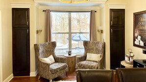 Une pièce comprenant deux fauteuils à motifs, un lustre, une fenêtre avec des rideaux et une citation encadrée accrochée au mur.