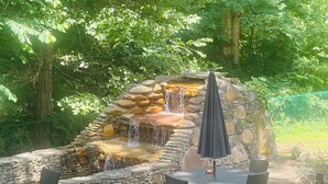 Une cascade artificielle en pierre, entourée d’un mur de pierre, avec une table et des chaises à proximité.