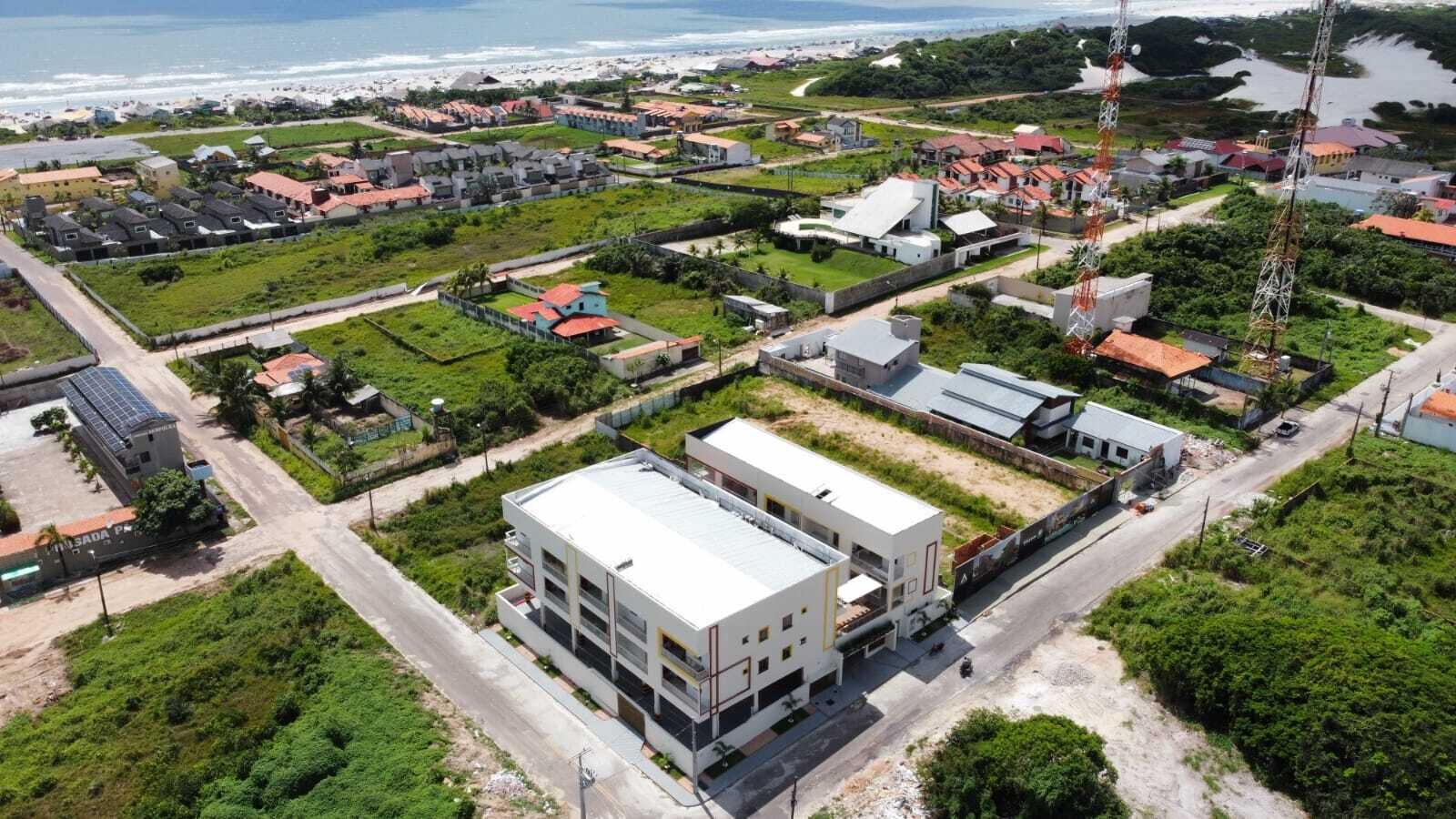 An aerial view of a coastal residential area with modern buildings, a large white structure with multiple floors, and a beach in the background.