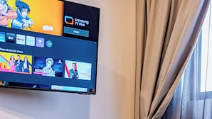 Una habitación de hotel moderna con un televisor de pantalla plana en la pared, una mesita auxiliar con una botella y un vaso, y una ventana con cortinas.