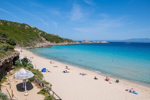 Ein Strand mit klarem türkisblauem Wasser, Sandstrand und felsigen Klippen.