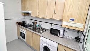Una cocina compacta con armarios de madera, microondas integrado, lavavajillas y un fregadero.
