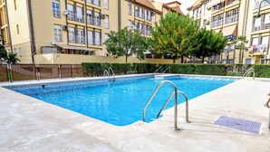 Una piscina con una escalera metálica, rodeada por un solárium con baldosas.