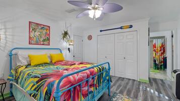 Un dormitorio con una colcha de colores, un ventilador de techo, un reloj de pared y una puerta con cortina colorida.