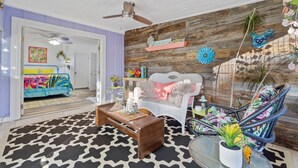 A living room with a wooden wall, a white sofa, a colorful chair, and a ceiling fan. - Charming 2-bedroom suite in soothing Navarre with AC, WiFi (Navarre)