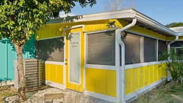 Un edificio amarillo con una puerta que dice "Tropical Blue", una ventana y un pequeño equipo de aire acondicionado.