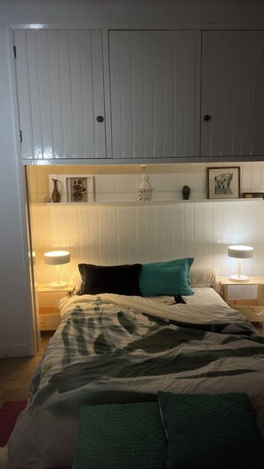 Un dormitorio con una cama, dos lámparas de noche, una mesita de noche y un estante con adornos.