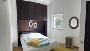 Ein Schlafzimmer mit Bett, Fenster, Heizkörper und Tür.