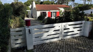 Ein weißes Tor mit einem roten Briefkasten, ein Kopfsteinpflasterweg und ein Haus mit rotem Dach und weißen Wänden.