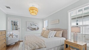 A bedroom with a bed, bedside tables, a dresser, a window with blinds, and a ceiling light fixture. - Pet Friendly Beach House - Hakuna Matata (Port St. Joe)