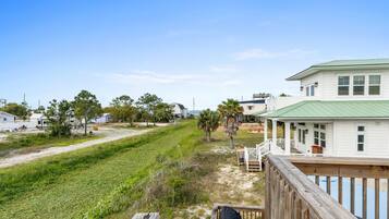 A coastal house with a green roof, a wooden deck, and a view of the beach.