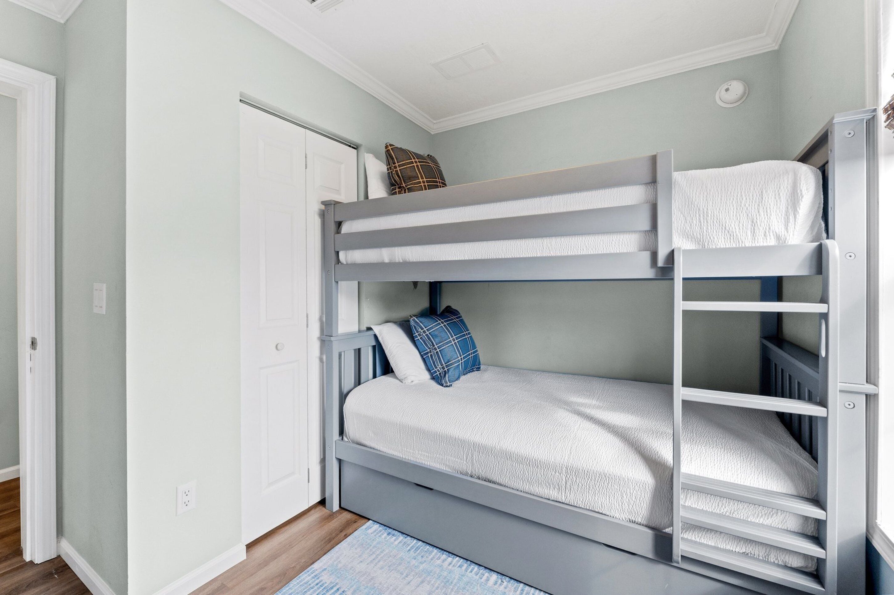 Une chambre avec un lit superposé, une porte, un mur blanc et un tapis bleu.