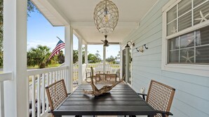 A covered porch with a dark wooden table and wicker chairs, an American flag, and a decorative ceiling light. - Pet Friendly Beach House - Hakuna Matata (Port St. Joe)