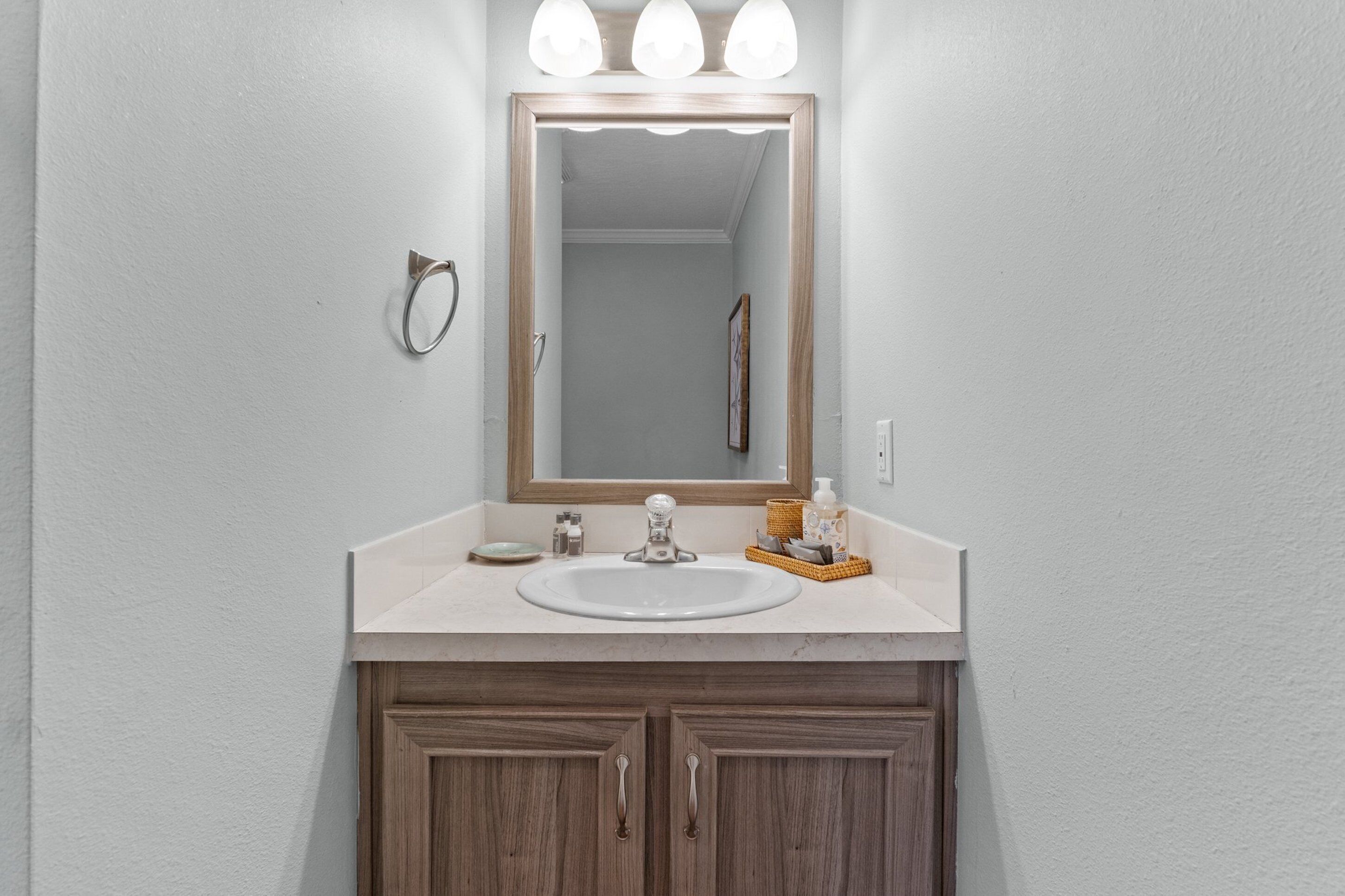 A bathroom with a white sink, wooden cabinets, a mirror with three lights, and toiletries on the counter.