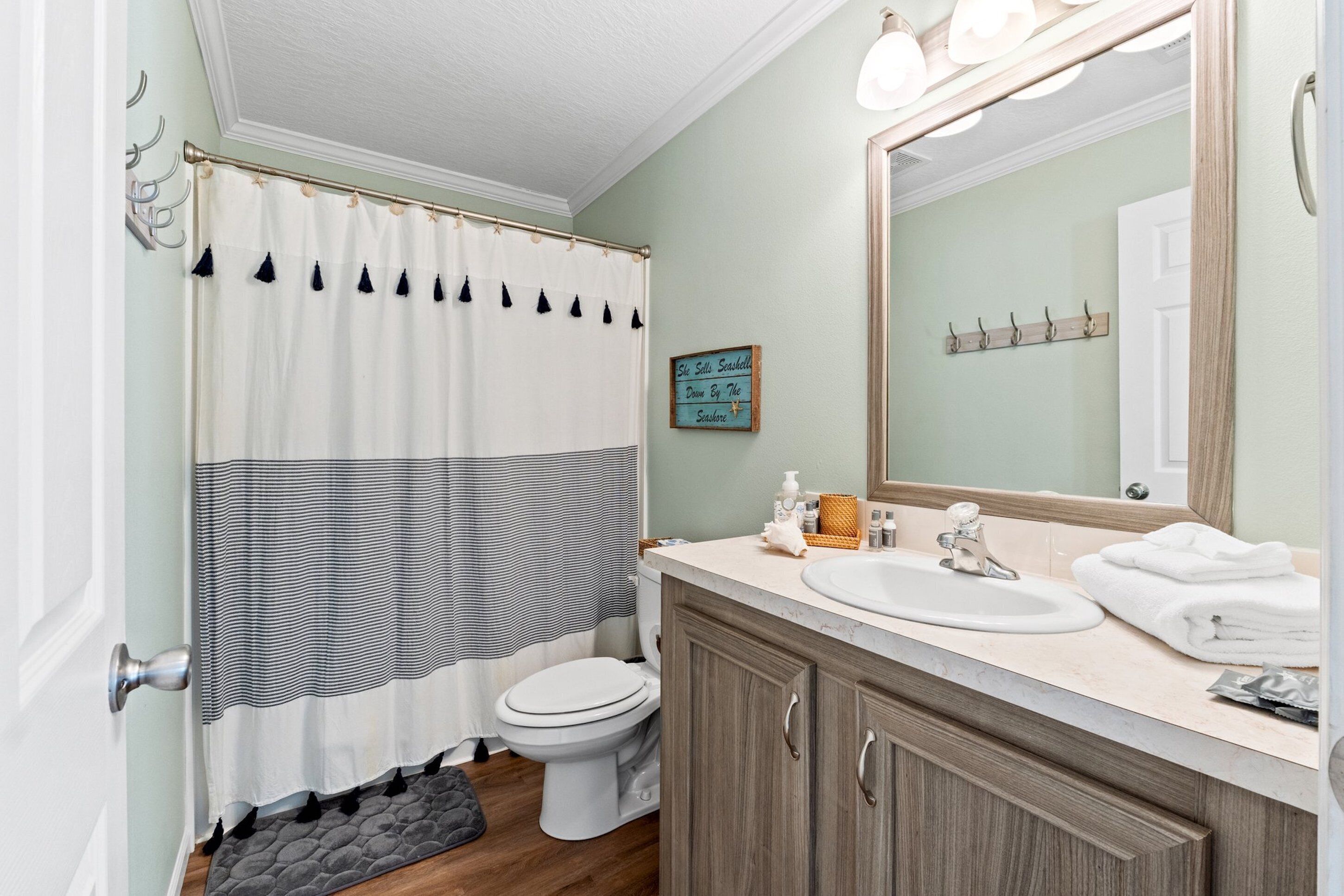 A bathroom with a white toilet, a beige sink, and a large mirror. There is a striped shower curtain and a small rug on the floor.