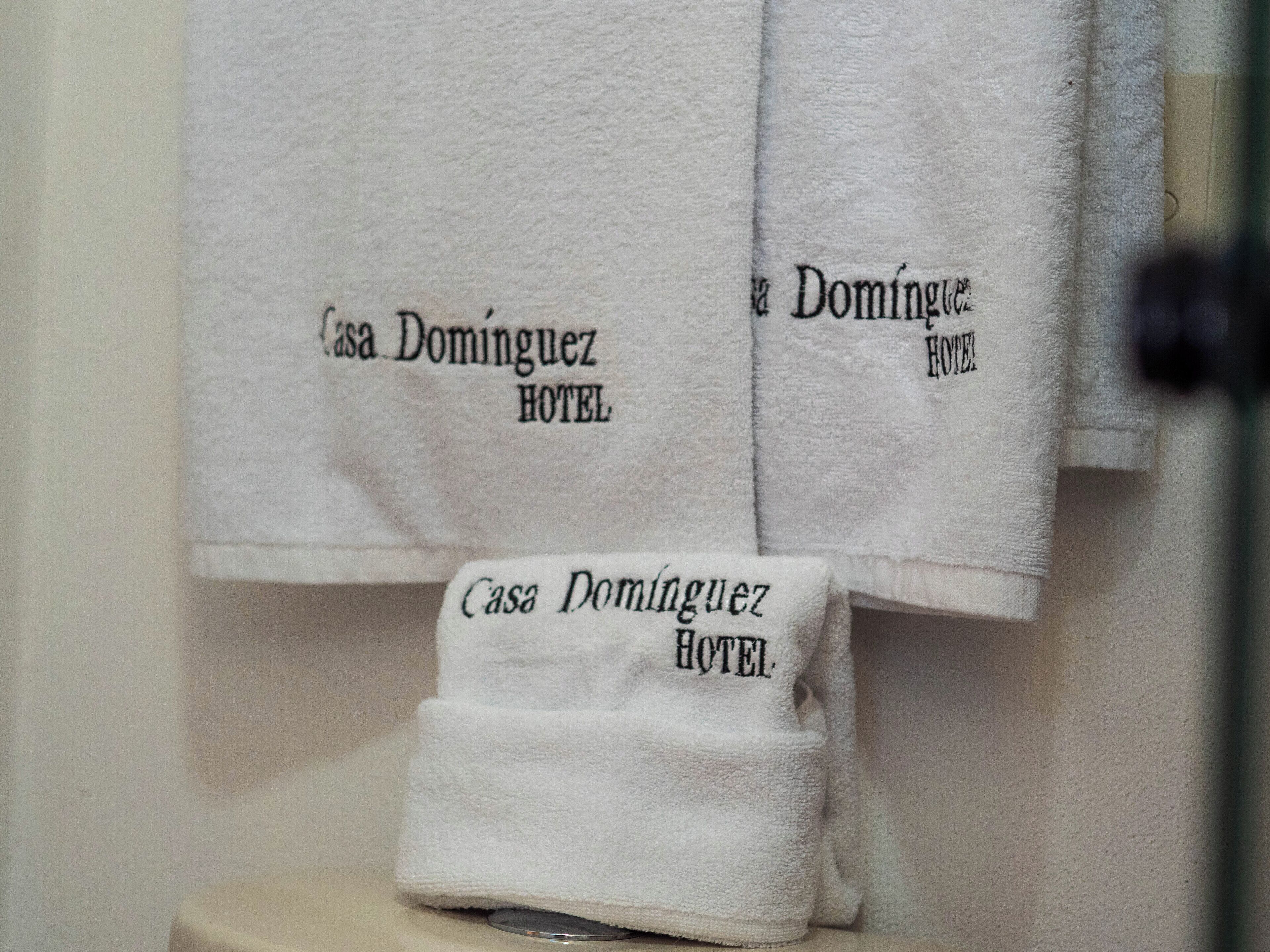 A bathroom with white towels hanging on a rack, each labeled "Casa Dominguez Hotel."