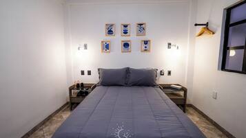 Habitación de hotel ordenada con una cama grande, una mesita de noche con lámpara y un aplique de pared.