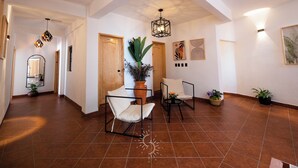 A spacious hallway with a high ceiling, geometric pendant lighting, a wooden door, and a seating area with a chair and table. - Hotel Casa Domínguez (Taxco)
