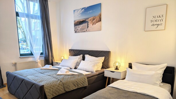 A double room with two beds, a window with sheer curtains, a bedside table with a globe lamp, and a motivational poster on the wall. - CaSa Apartment East Field - 5 beds, family-friendly, fully equipped (Magdeburg)