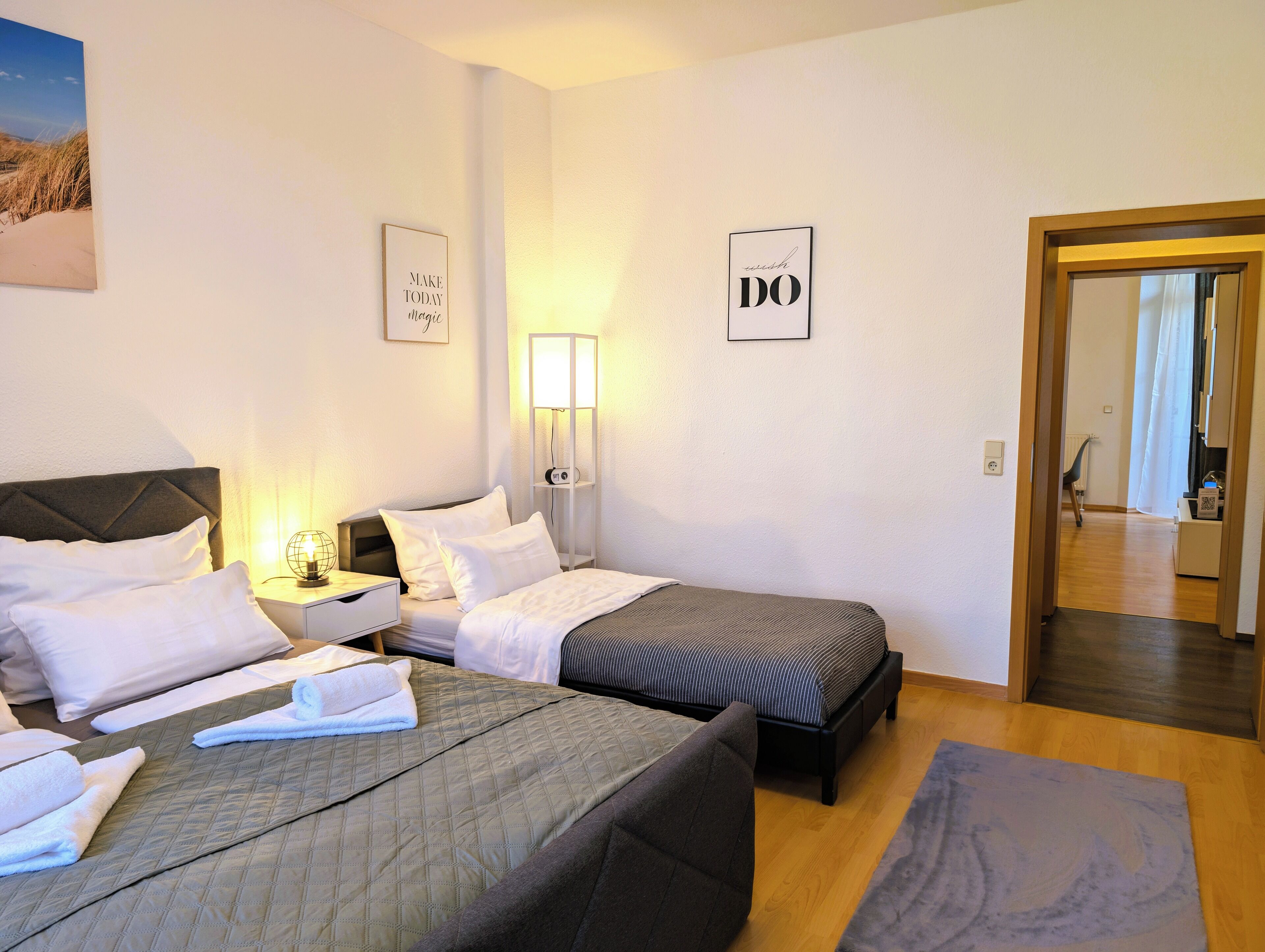 Habitación de hotel con dos camas, una mesita de noche con lámpara y una repisa en la pared.