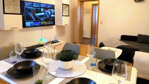 A modern hotel room with a dining area set for two, a flat-screen TV mounted on the wall, and a cozy seating area with a sofa. - CaSa Apartment East Field - 5 beds, family-friendly, fully equipped (Magdeburg)