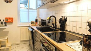 A modern kitchen with a black stove, a sink, and a window with blinds. - CaSa Apartment East Field - 5 beds, family-friendly, fully equipped (Magdeburg)