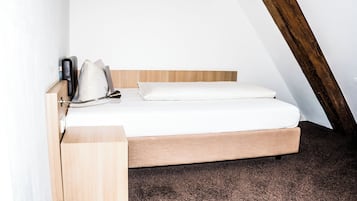 A single bed with a wooden frame and white bedding in a room with sloped ceilings and a brown carpet.