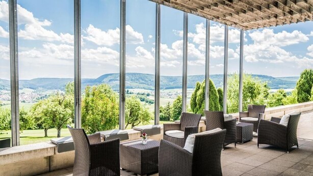 An outdoor patio with wicker furniture and a view of a green landscape. - Hotel Hofgut Hohenkarpfen (Hausen ob Verena)