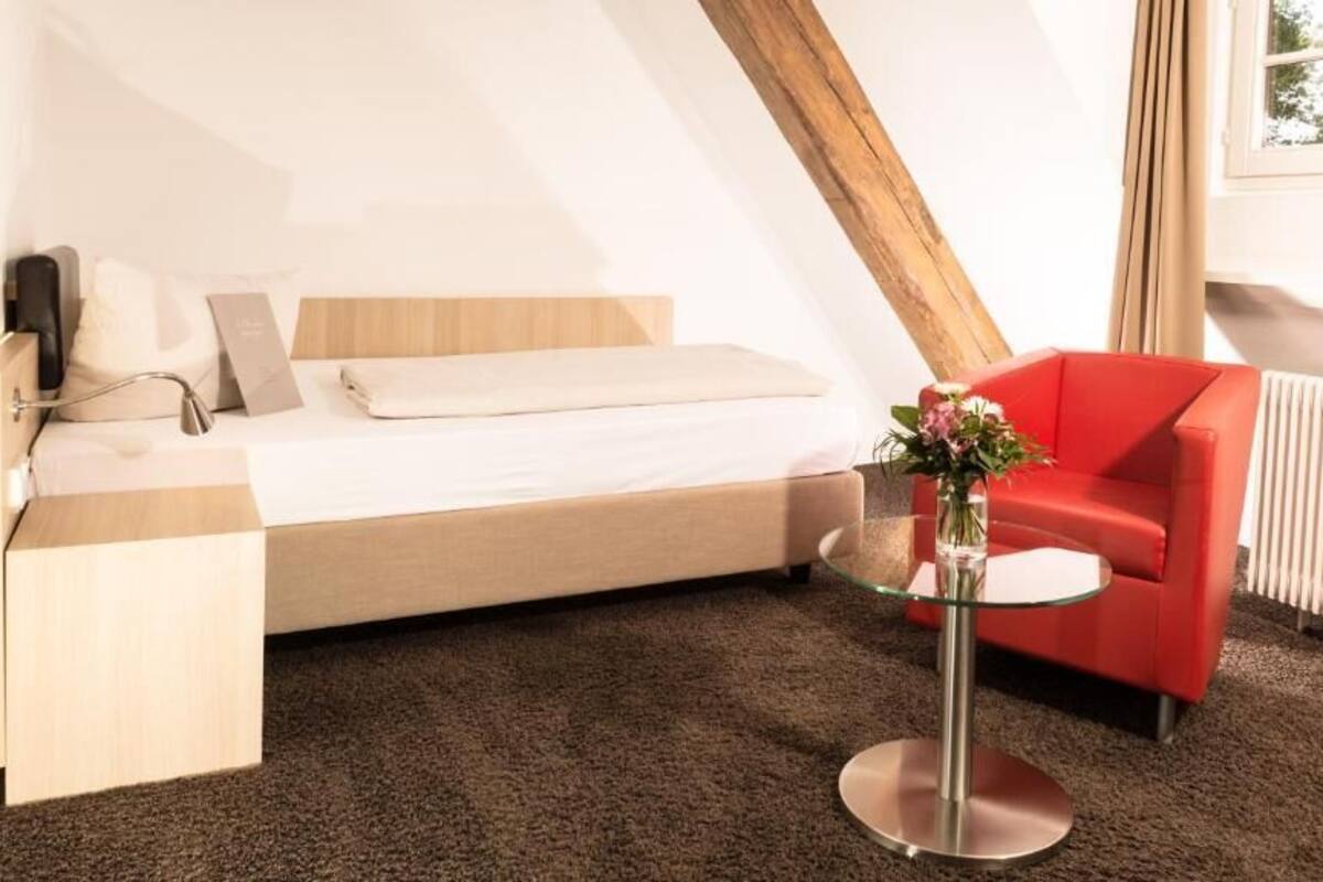 Une chambre moderne avec un lit en mezzanine, un fauteuil rouge, une petite table avec un vase de fleurs et un radiateur.