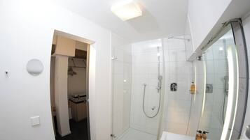 A modern bathroom with a glass-enclosed shower, a white sink with toiletries, and a walk-in closet.