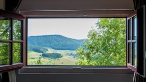 A room with a large window offering a view of a green landscape with trees and hills. - Hotel Hofgut Hohenkarpfen (Hausen ob Verena)