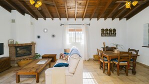 Un salon doté d’une cheminée, d’un plafond en bois et d’un coin repas avec des chaises et une table.