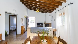 Un salon chaleureux avec un plafond en bois, une cheminée, un téléviseur et un coin repas comprenant une table et des chaises.