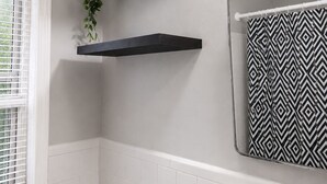 Een badkamer met witte betegelde wanden, een handdoek met zwart-wit patroon en een plant op een zwart schap.