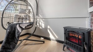 Een kamer met een hangstoel, een zwart houtkacheltje en een raam met zonwering.