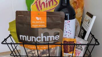 A shopping basket containing a bottle of wine, a bag of roasted almonds, a packet of munchme snacks, a pack of Thins potato chips, and a bar snack package.
