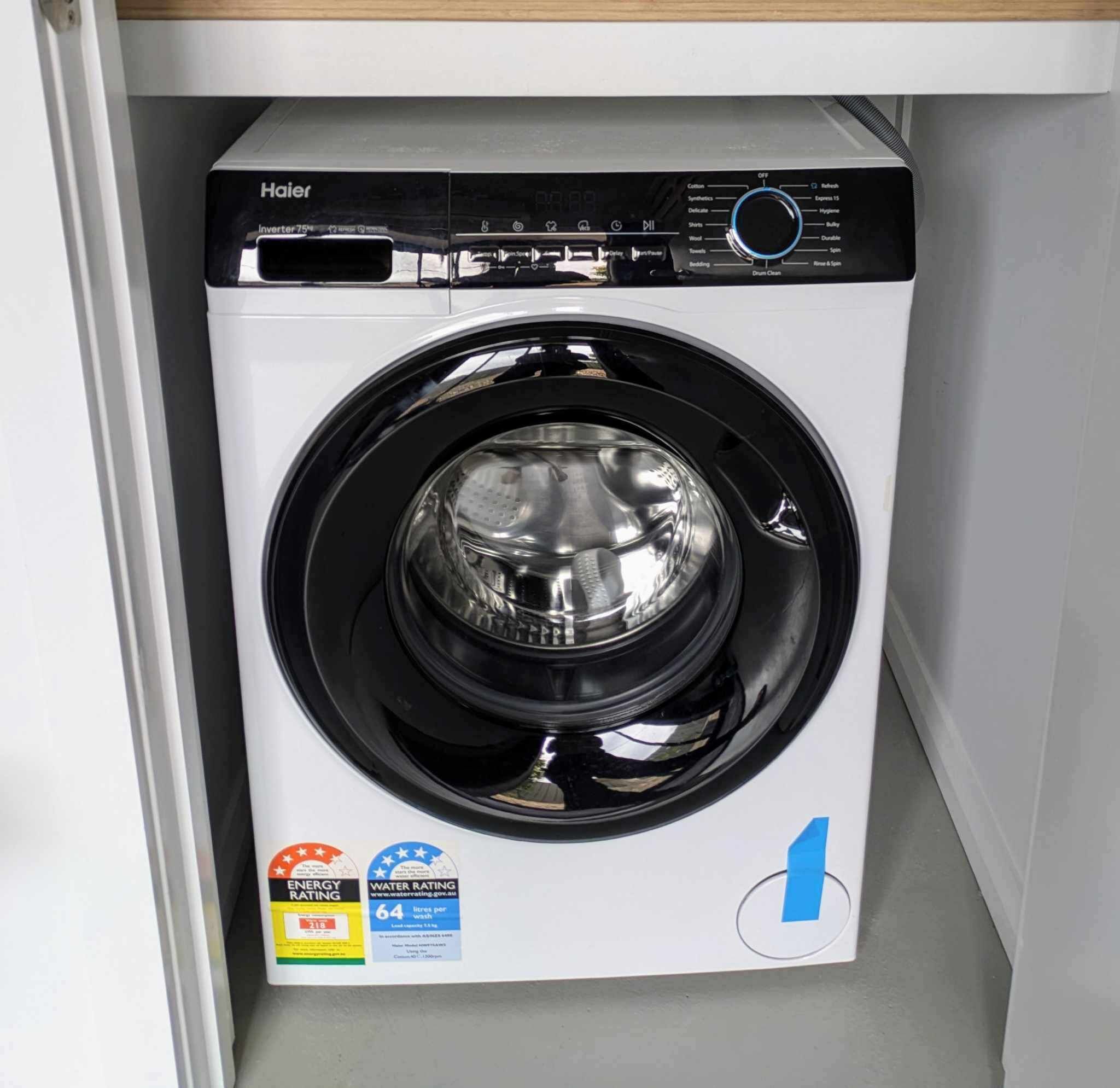 Una lavatrice Haier a carica frontale con pannello di controllo digitale, etichette per l'efficienza energetica e il consumo di acqua, e un simbolo blu del riciclo.
