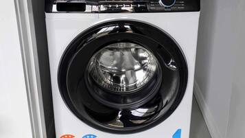 Una lavatrice Haier a carica frontale con pannello di controllo digitale, etichette per l'efficienza energetica e il consumo di acqua, e un simbolo blu del riciclo.