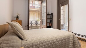 A bedroom with a bed, a wooden headboard, a bedside table with a plant, and a view of a balcony with a railing. - PURE GRACIA, 2 bedrooms, excellent location (Barcelona)