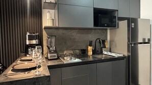 Cozinha moderna com armários escuros, micro-ondas embutido, geladeira de aço inoxidável e cafeteira.