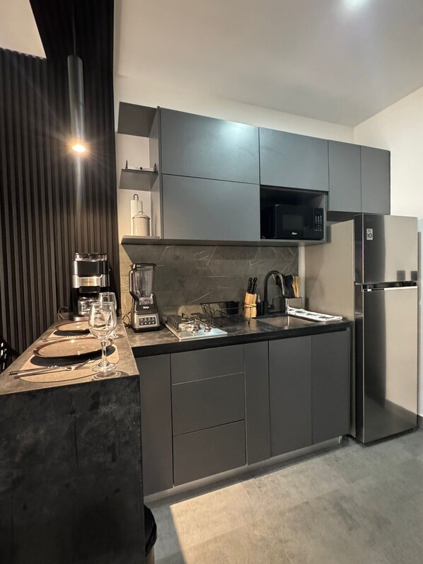 Een moderne keuken met donkere kasten, een ingebouwde magnetron, een roestvrijstalen koelkast en een koffiezetapparaat.