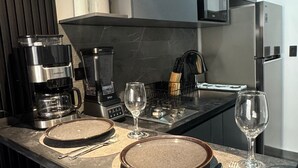 Cozinha moderna com fogão embutido, máquina de café e micro-ondas. Duas mesas de jantar montadas com pratos e talheres.