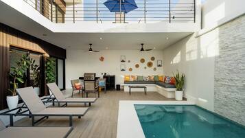 Un espacio exterior moderno con piscina, sillones de descanso, zona de barbacoa y comedor.