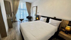 A hotel room with a large bed, a desk, a chair, a bedside lamp, and a view of the outdoors through sheer curtains. - Cozy Stay + breakfast 201 (Addis Ababa)