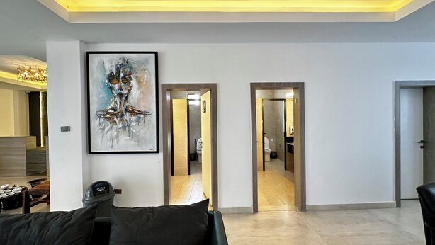 A modern living room with a large abstract painting, a sofa, and a coffee table. There are two doors leading to other rooms. - Cozy Stay + breakfast 201 (Addis Ababa)