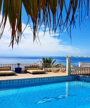 Piscina com vista clara do oceano, cerca branca e alguns cadezões de praia.